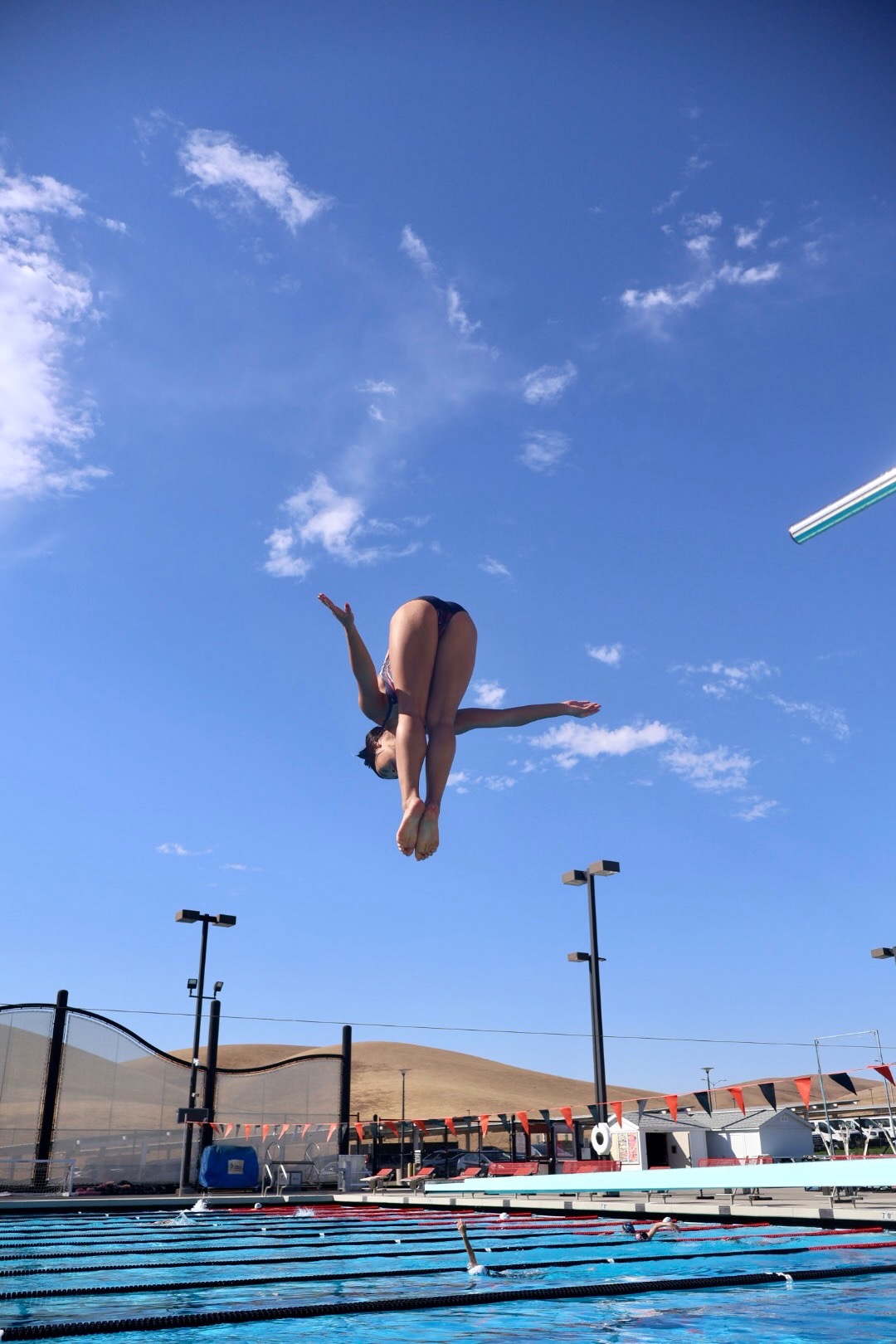 High school diver in tuck position high above the pool at Las Positas