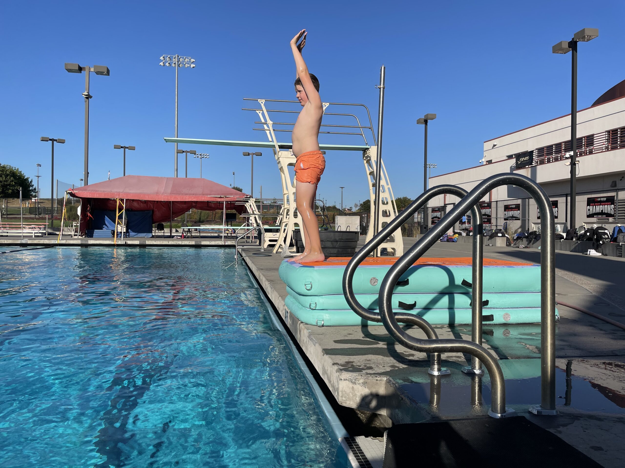 A diver in arms-up streamline position at the edge of the board during a one-on-one session