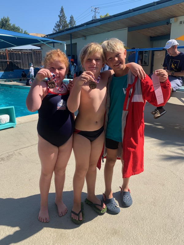 Three young TVD divers showing off their medals and ribbon at a meet